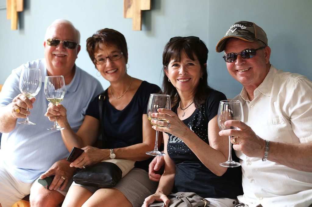 Two couples smile at the camera and toast with white wine